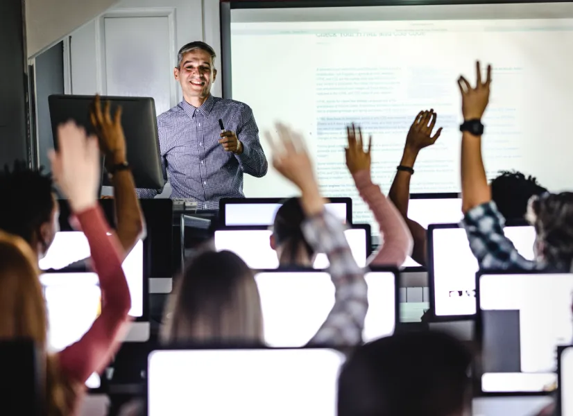 Teacher in front of a classroom with students raising their hands