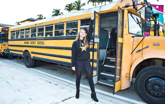 Student in a Hamilton sweater doing the Hamilton pose in front of a school bus