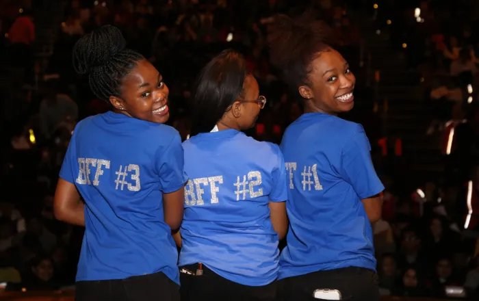 Three girls on stage in blue shirt looking backwards and smiling
